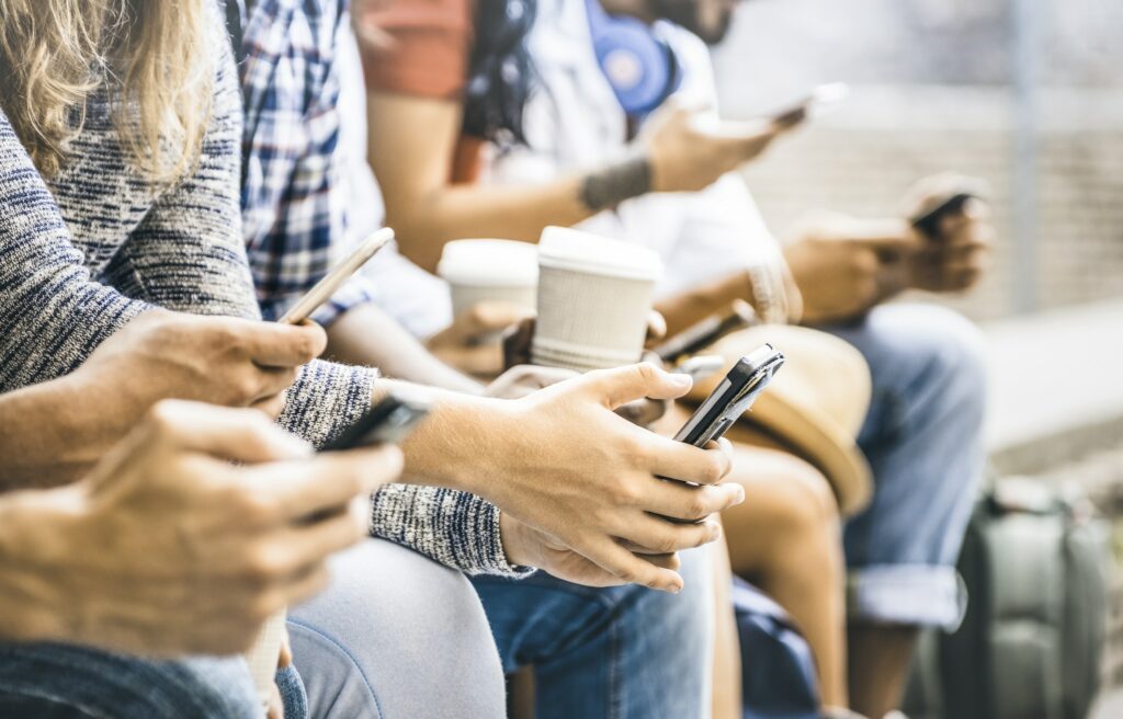 Multiple people sitting at a bench, using their phones or holding coffee cups