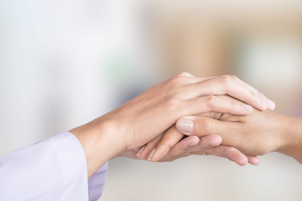 Doctor wrapping hand around patient’s hand to show empathy