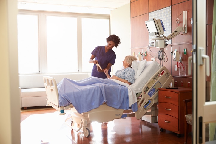 Agency nurse speaking to patient in hospital bed