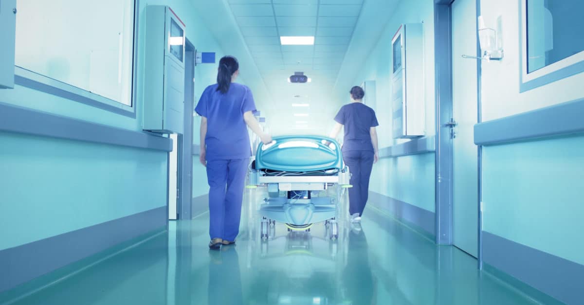 Nurses walking hospital bed through hallway