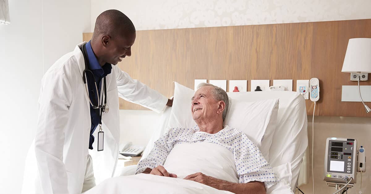 Doctor Visiting And Talking With Senior Male Patient In Hospital Bed