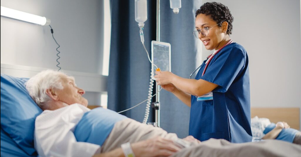 Friendly Female Head Nurse Making Rounds does Checkup on Elderly Patient Resting in Bed.